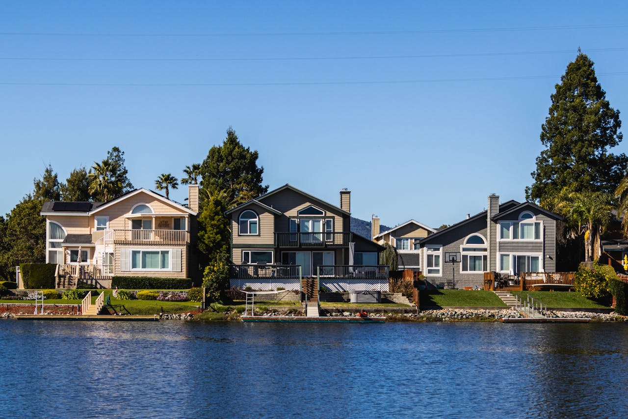 Charming lakeside houses reflect on calm waters under a clear blue sky.