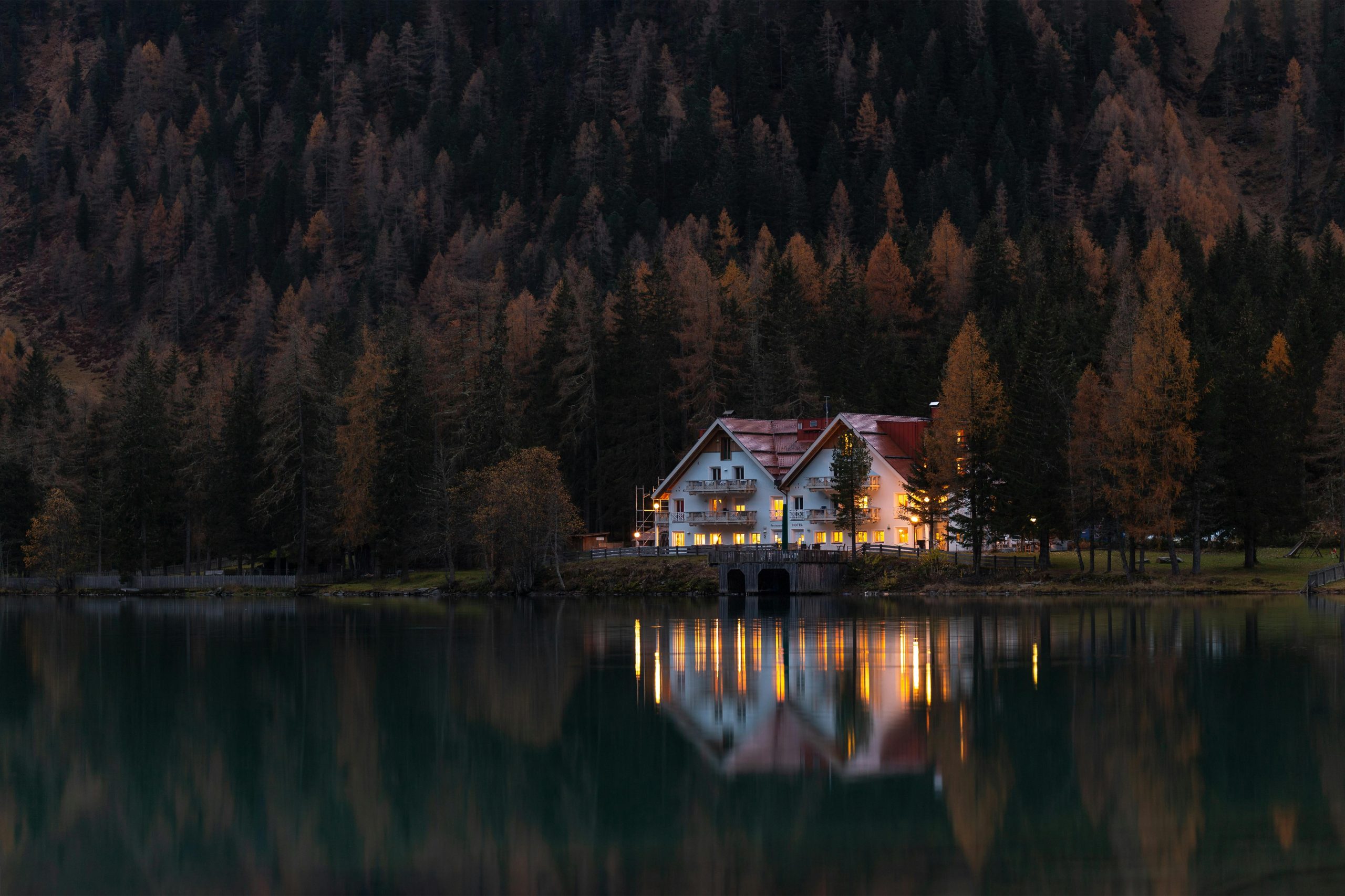 Scenic autumn view of a lakeside house reflecting on calm waters at twilight.